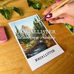 May include: A watercolor painting of a mountain landscape with a river flowing through it. The painting is on a white card with the text "Macallister Painting Names" and "Macallister" written on it.