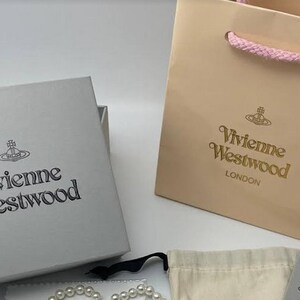 Op de afbeelding: Twee dozen met het Vivienne Westwood logo, de ene is een lichtgrijze doos en de andere is een lichtroze doos. De roze doos heeft een roze lintje als handvat.