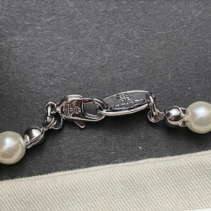 Op de afbeelding: Een zilveren ketting met een zilveren sluiting en witte nepparels. De sluiting heeft het Vivienne Westwood logo.