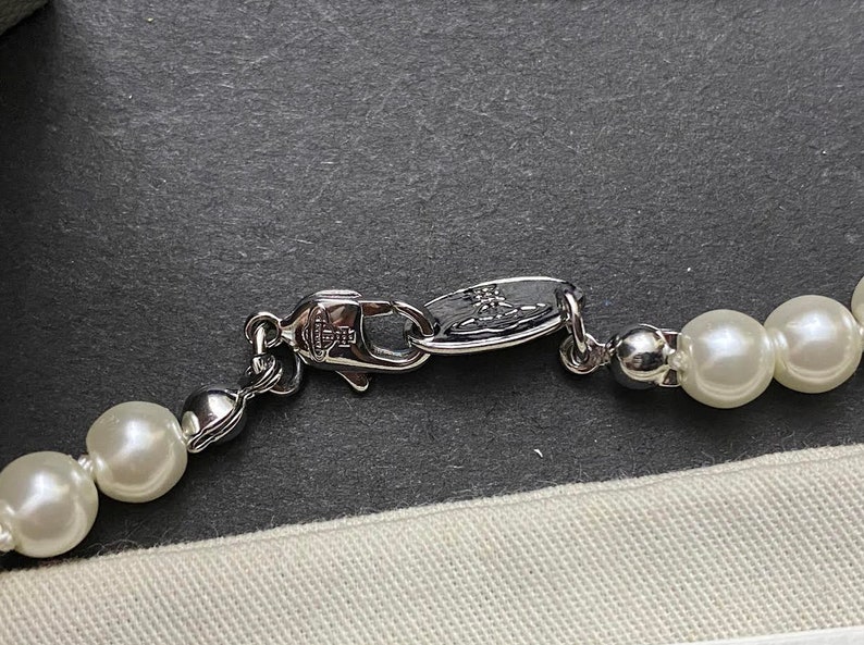 Op de afbeelding: Een zilveren ketting met een zilveren sluiting en witte nepparels. De sluiting heeft het Vivienne Westwood logo.