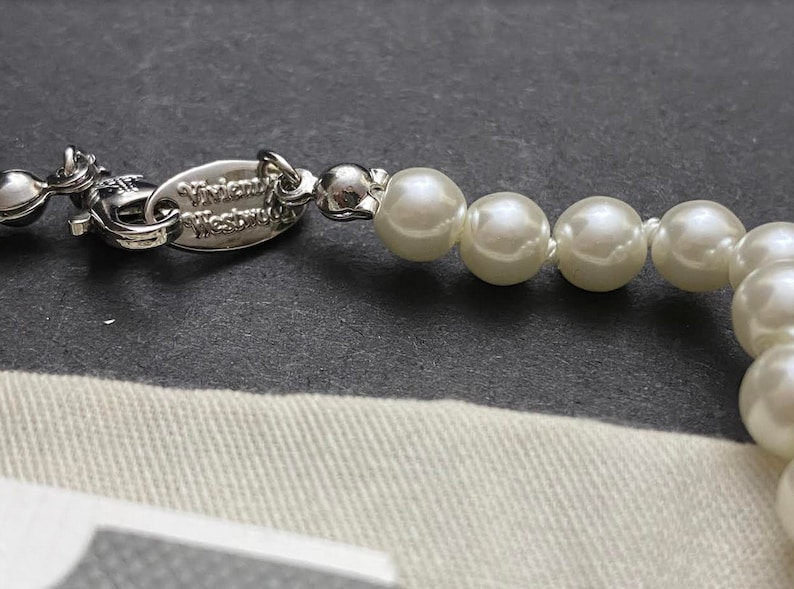 Op de afbeelding: Een zilveren ketting met een Vivienne Westwood-label en witte nepparel kralen.