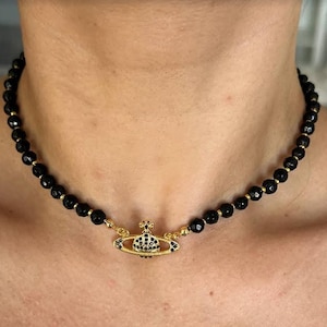 May include: A black beaded choker necklace with a gold orb pendant featuring black crystal accents.