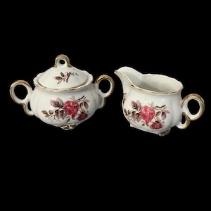 May include: A white porcelain creamer and sugar bowl set with a pink rose floral design and gold trim.