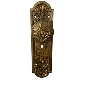 Pode incluir: Maçaneta de porta antiga em latão dourado com um puxador redondo ornamentado e uma placa traseira retangular. O puxador apresenta um design floral em espiral, e a placa traseira tem uma superfície texturizada e detalhes florais. Ferragens vintage.