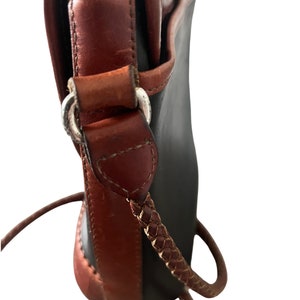 May include: A black and brown leather shoulder bag with a braided strap. The bag has a flap closure and a silver buckle.