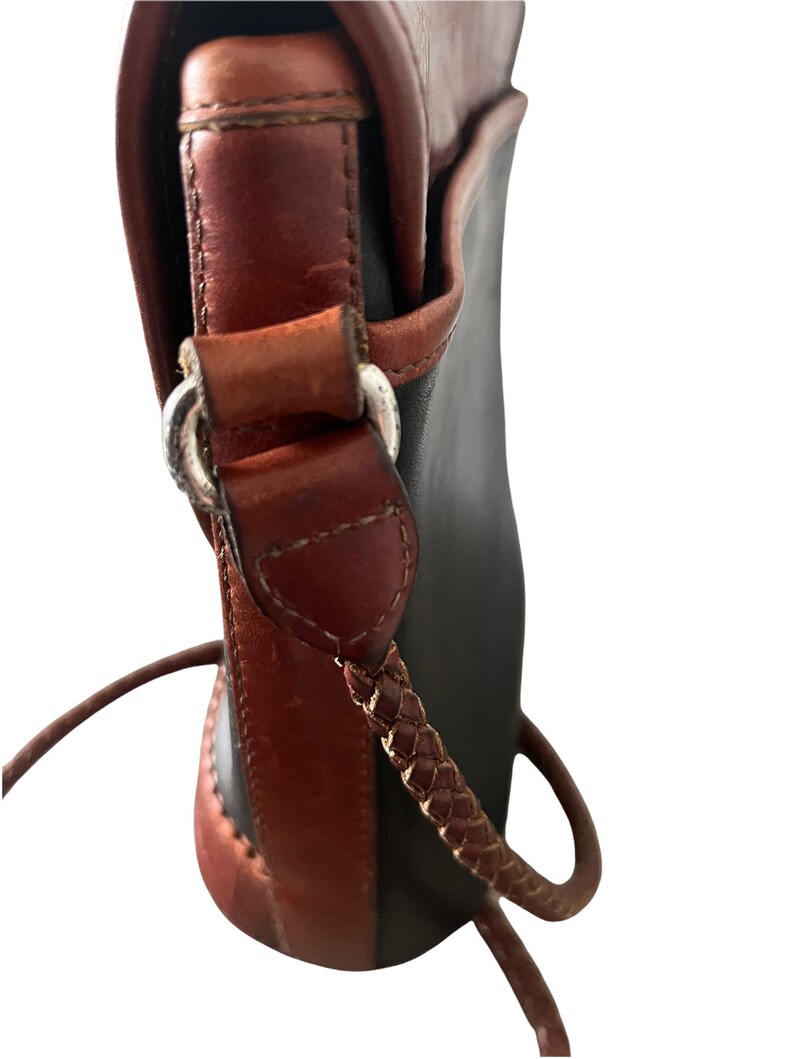 May include: A black and brown leather shoulder bag with a braided strap. The bag has a flap closure and a silver buckle.