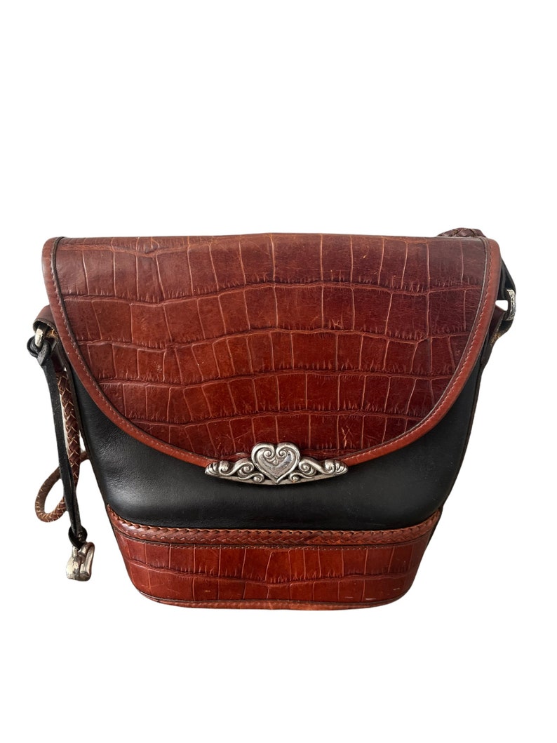 May include: A brown leather crossbody bag with a black leather flap and a silver heart-shaped buckle. The bag has a crocodile-embossed pattern.