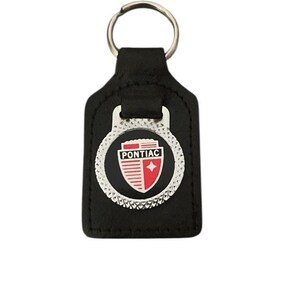 May include: Black leather keychain with a silver key ring. The keychain features a silver emblem with the word "PONTIAC" above a red and white shield logo.
