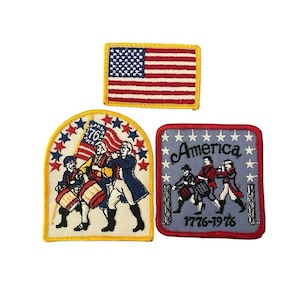 Puede incluir: Tres parches bordados con temas patrióticos. Uno muestra la bandera estadounidense. Los otros dos parches representan figuras con vestimenta colonial, uno de ellos con la inscripción "America 1776-1976". Los parches son rojos, blancos, azules y amarillos.