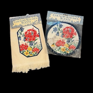 May include: A cream-colored kitchen towel with a floral design and fringe, alongside a matching round pot holder. Both items feature red, yellow, and blue flowers, with the text "COUNTRY KITCHEN SCENTS" on the packaging.