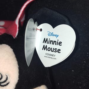 May include: A Minnie Mouse plush toy with a red and white polka dot bow. The heart-shaped tag reads "Disney Minnie Mouse" and includes the Disney logo and website.