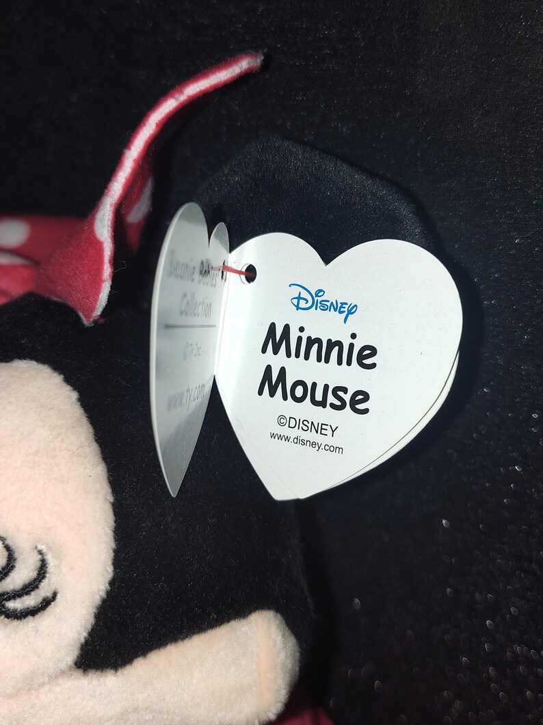May include: A Minnie Mouse plush toy with a red and white polka dot bow. The heart-shaped tag reads "Disney Minnie Mouse" and includes the Disney logo and website.