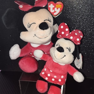 May include: Two Minnie Mouse plush toys. The larger one has a red dress and a red bow with white polka dots. The smaller one has a red dress with white polka dots and a matching bow. Both have black ears and closed eyes.