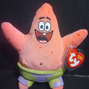 May include: A plush toy of Patrick Star from the animated series Spongebob Squarepants. The pink starfish character has a smiling face, orange spots, and is wearing green and purple shorts. A red heart-shaped Ty Beanie Babies tag is attached.