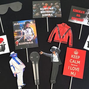 May include: A collection of Michael Jackson themed party photo booth props on sticks, including a red jacket, a microphone, sunglasses, and rectangular signs with text like Happy 8th Birthday Kimora and Keep Calm Because I Love MJ.