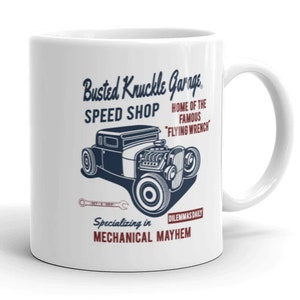 Puede incluir: Taza de cerámica blanca con un gráfico azul y rojo de un coche de carreras vintage y el texto "Busted Knuckle Garage. Speed Shop Home of the Famous "Flying Wrench" Dilemmas Daily Specializing in Mechanical Mayhem"