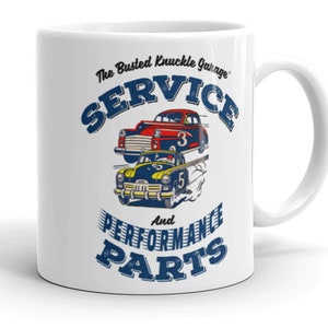Puede incluir: Taza de cerámica blanca con una ilustración azul, roja y amarilla de dos coches antiguos. El texto "The Busted Knuckle Garage" está en la parte superior, y "SERVICE" está en un círculo azul grande. Debajo de los coches está el texto "And PERFORMANCE PARTS".