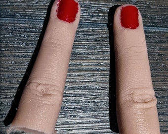 May include: Two realistic-looking fingertip props with red nail polish. The fingertips are made of a flesh-toned silicone material.