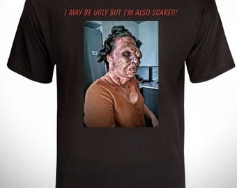 May include: Black t-shirt with the text "I may be ugly but I'm also scared!" and a photo of a woman with a grotesque makeup design.