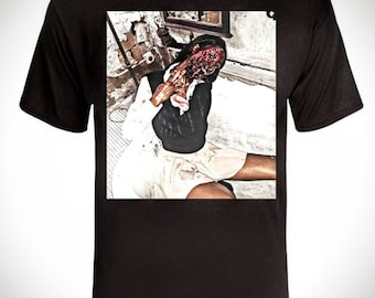 May include: Black t-shirt with a graphic print of a person with a bloody face and a white skirt. The person is sitting on a floor with a brick wall in the background.