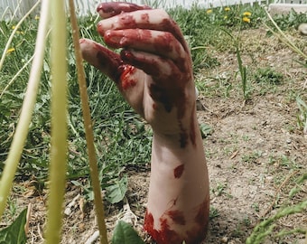 May include: A bloody hand and forearm sticking out of the ground, covered in dirt and grass.