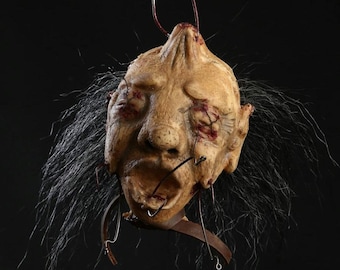 May include: A realistic, detailed, and disturbing prop of a human head with stitched-up eyes and mouth, hanging from a metal hook. The head is covered in fake blood and has a realistic texture.