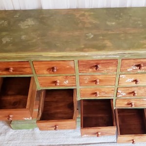 May include: A green painted wooden cabinet with 12 drawers. The drawers are open and empty. The cabinet has a distressed look with a green paint finish.