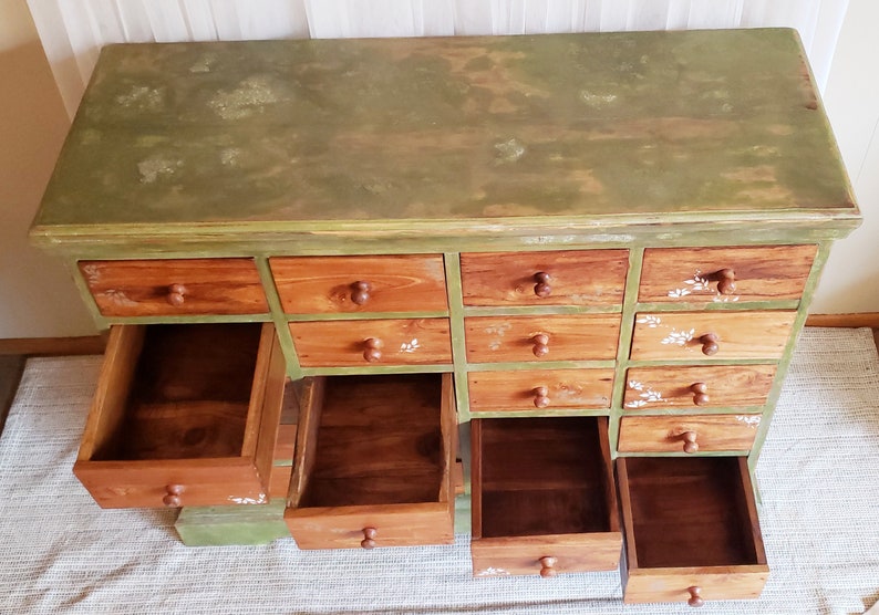 May include: A green painted wooden cabinet with 12 drawers. The drawers are open and empty. The cabinet has a distressed look with a green paint finish.