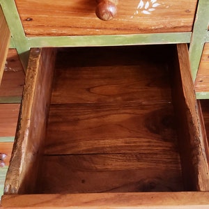 May include: A wooden dresser with multiple drawers. The drawers are painted green and have wooden knobs. The dresser is made of natural wood with a rustic finish.