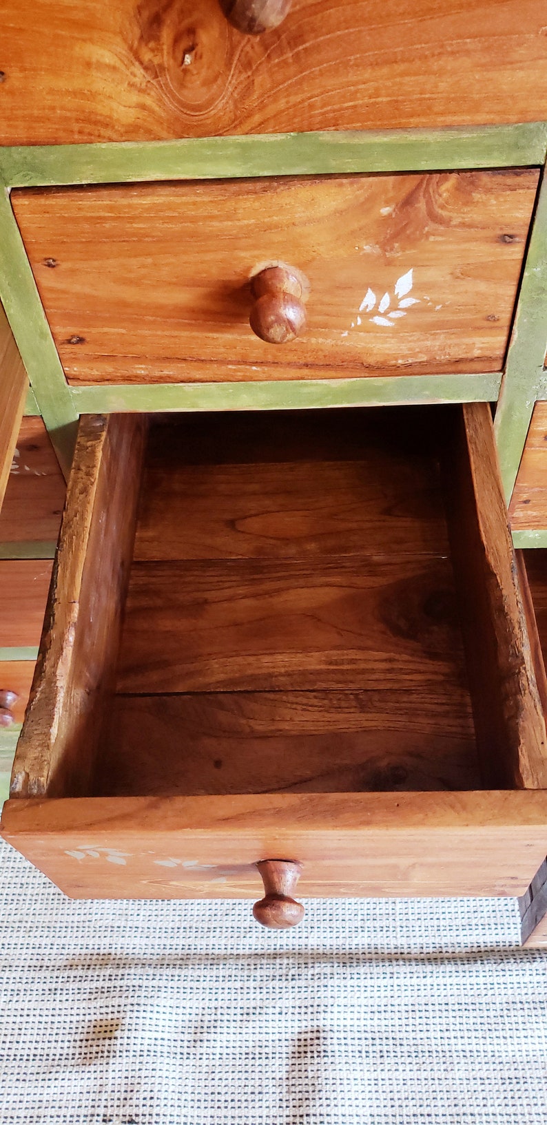 May include: A wooden dresser with multiple drawers. The drawers are painted green and have wooden knobs. The dresser is made of natural wood with a rustic finish.