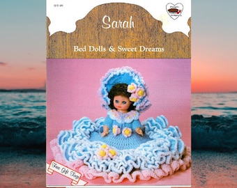 May include: A crochet pattern for a bed doll named Sarah. The doll is wearing a blue and pink dress with a matching hat. The pattern includes free gift tags.