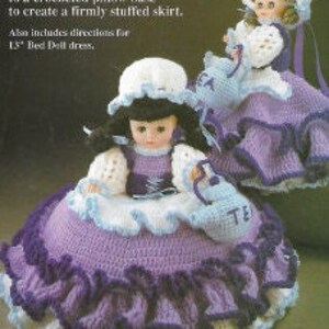 K&ouml;nnte beinhalten: Eine geh&auml;kelte Kissenpuppe mit einem lila Rock und einem wei&szlig;en Oberteil. Die Puppe h&auml;lt eine Teekanne und tr&auml;gt einen wei&szlig;en Hut. Die Puppe ist 26,5 cm gro&szlig; und enth&auml;lt Anleitungen f&uuml;r ein 38 cm gro&szlig;es Bettpuppenkleid.