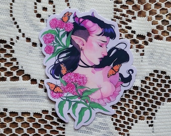 May include: A sticker featuring a fantasy illustration of a person with pink skin, black hair, and horns. The person is surrounded by pink flowers and orange butterflies. The sticker has a white border.
