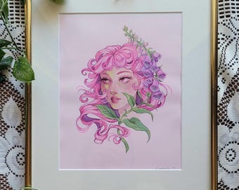May include: A framed art print featuring a stylized illustration of a person with flowing pink hair adorned with purple foxglove flowers and green leaves. The artwork is set against a soft pink background and enclosed in a thin gold metal frame.