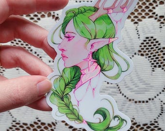 May include: A sticker featuring a side profile of a fantasy character with green hair, antlers, and pointed ears. The character has pink skin and is wearing a pink star-shaped earring. The sticker has a white border.