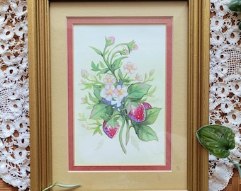 May include: A framed watercolor painting featuring a botanical illustration of strawberries, green leaves, and small white and pink flowers. The artwork is encased in a gold-toned wooden frame with a cream-colored mat and a thin red inner border.