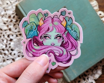 May include: A sticker featuring a green-skinned, pink-haired creature with horns and a floral background. The creature has large, expressive eyes and is surrounded by leaves and hearts.