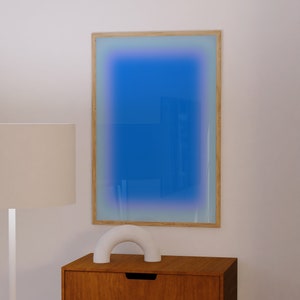 May include: A wooden framed mirror with a blue gradient background. The mirror is hanging on a white wall above a wooden dresser with two drawers. A white ceramic arch sculpture is sitting on top of the dresser.