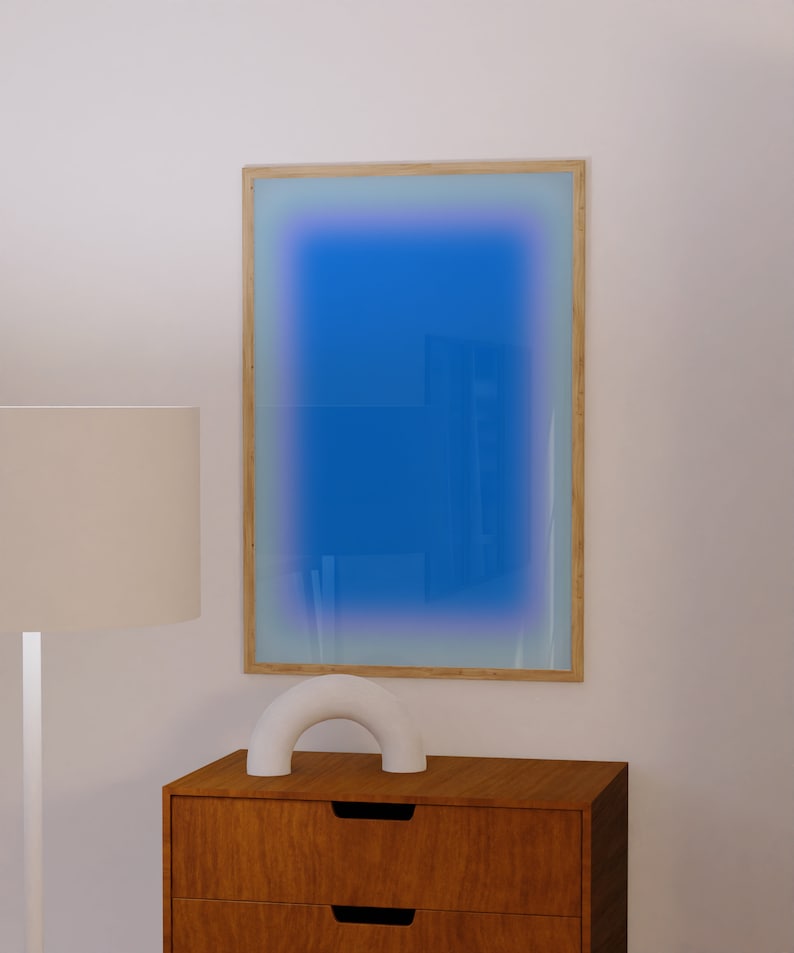 May include: A wooden framed mirror with a blue gradient background. The mirror is hanging on a white wall above a wooden dresser with two drawers. A white ceramic arch sculpture is sitting on top of the dresser.