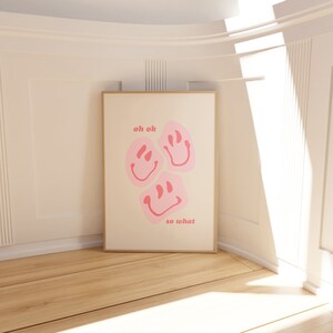 May include: A white poster with a gold frame features three pink smiley faces with the text "oh ok" and "so what" in pink.