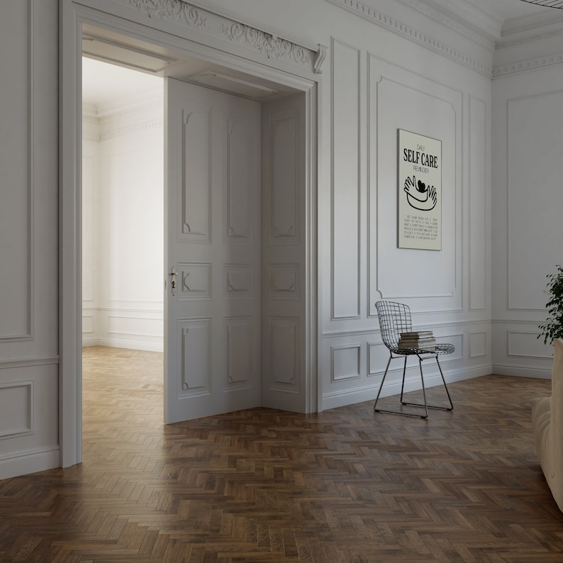 May include: A white room with a wooden herringbone floor. A white door is open to reveal another white room. A white framed poster with the text "Daily Self Care Reminders" hangs on the wall. A black and white illustration of two hands holding a heart is on the poster. A wire chair with a stack of books sits in the corner of the room.