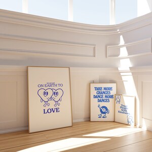 May include: Three framed prints with blue and white illustrations and text. The first print says "We are put on Earth to LOVE" and features two cartoon hearts holding hands. The second print says "TAKE MORE CHANCES DANCE MORE DANCES" and features a cartoon figure dancing with a record player. The third print says "Treat People With Kindness" and features a cartoon heart with a smiley face.