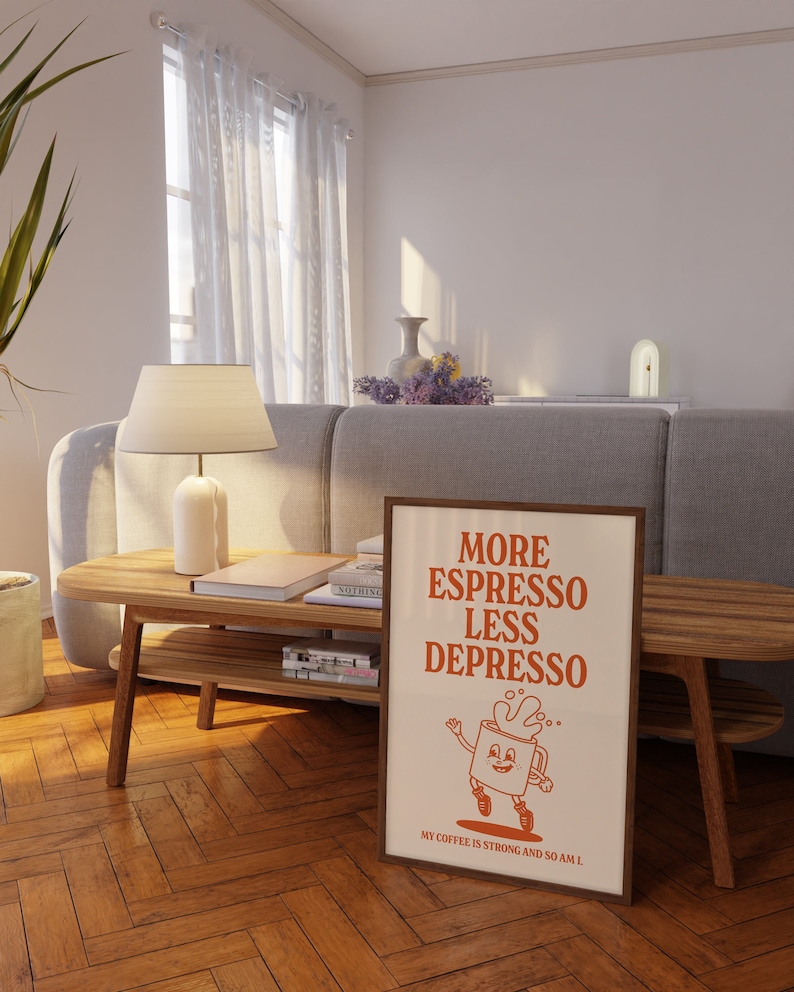 May include: A framed poster with the text "MORE ESPRESSO LESS DEPRESSO" in orange. The poster features a cartoon coffee cup character. The poster is displayed in a living room setting with a wooden coffee table and a gray sofa.