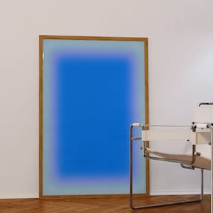 May include: A framed abstract art print with a blue gradient background and a wooden frame. The print is hanging on a white wall next to a white chair.