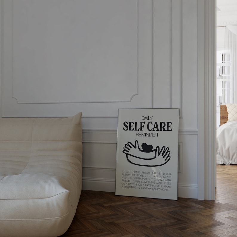 May include: A white framed poster with black text that reads "Daily Self Care Reminder". The poster features a black and white illustration of two hands holding a heart. The poster lists 10 self-care tips.