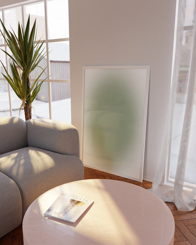May include: A light gray sectional sofa with a pink round coffee table and a magazine on top. A green and white abstract painting hangs on the wall behind the sofa. A large green plant is in the corner of the room.
