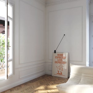 May include: A framed poster with the text "MORE ESPRESSO LESS DEPRESSO" hangs on a white wall. The poster features a cartoon coffee cup character. The room has a white chair, a window, and a wooden floor.