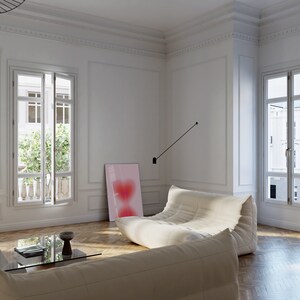 May include: A white sectional sofa with a pink abstract painting on the wall behind it. The sofa is in a room with white walls and hardwood floors. There is a glass coffee table in front of the sofa.