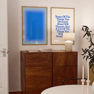 May include: Two framed prints on a white wall above a wooden cabinet. The print on the left is a blue gradient. The print on the right has the text "Some Of The Things You Dreamed About Will Happen And A Lot Of The Things You Wor About".