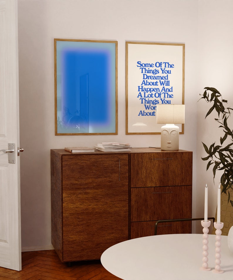 May include: Two framed prints on a white wall above a wooden cabinet. The print on the left is a blue gradient. The print on the right has the text "Some Of The Things You Dreamed About Will Happen And A Lot Of The Things You Wor About".